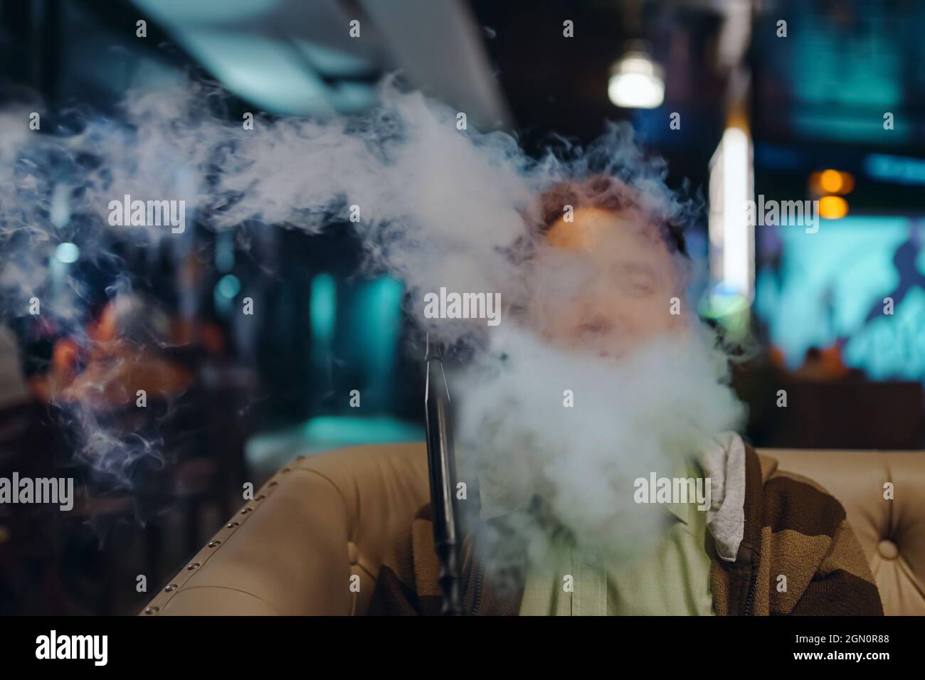 Portrait d'un jeune homme dans la fumée. Détendez-vous au bar shisha. Homme au restaurant fumant le narguilé. Personne sur le canapé dans le café. Banque D'Images