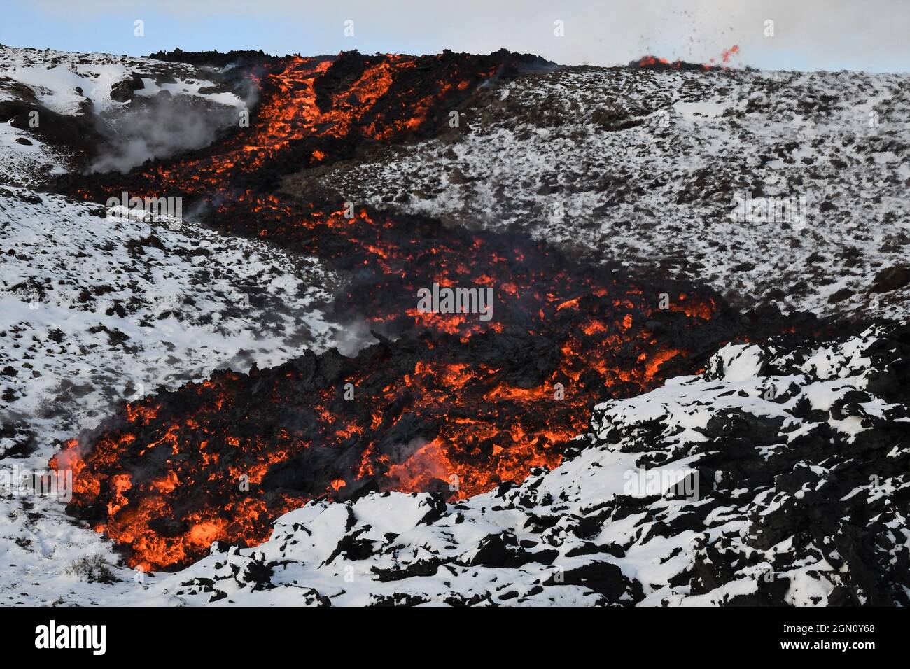 Coulée de lave à Faggadalsfjall, Islande. La lave rouge et orange fondue avec une croûte noire refroidie s'écoule sur une colline blanche et enneigée en zigzag. Banque D'Images