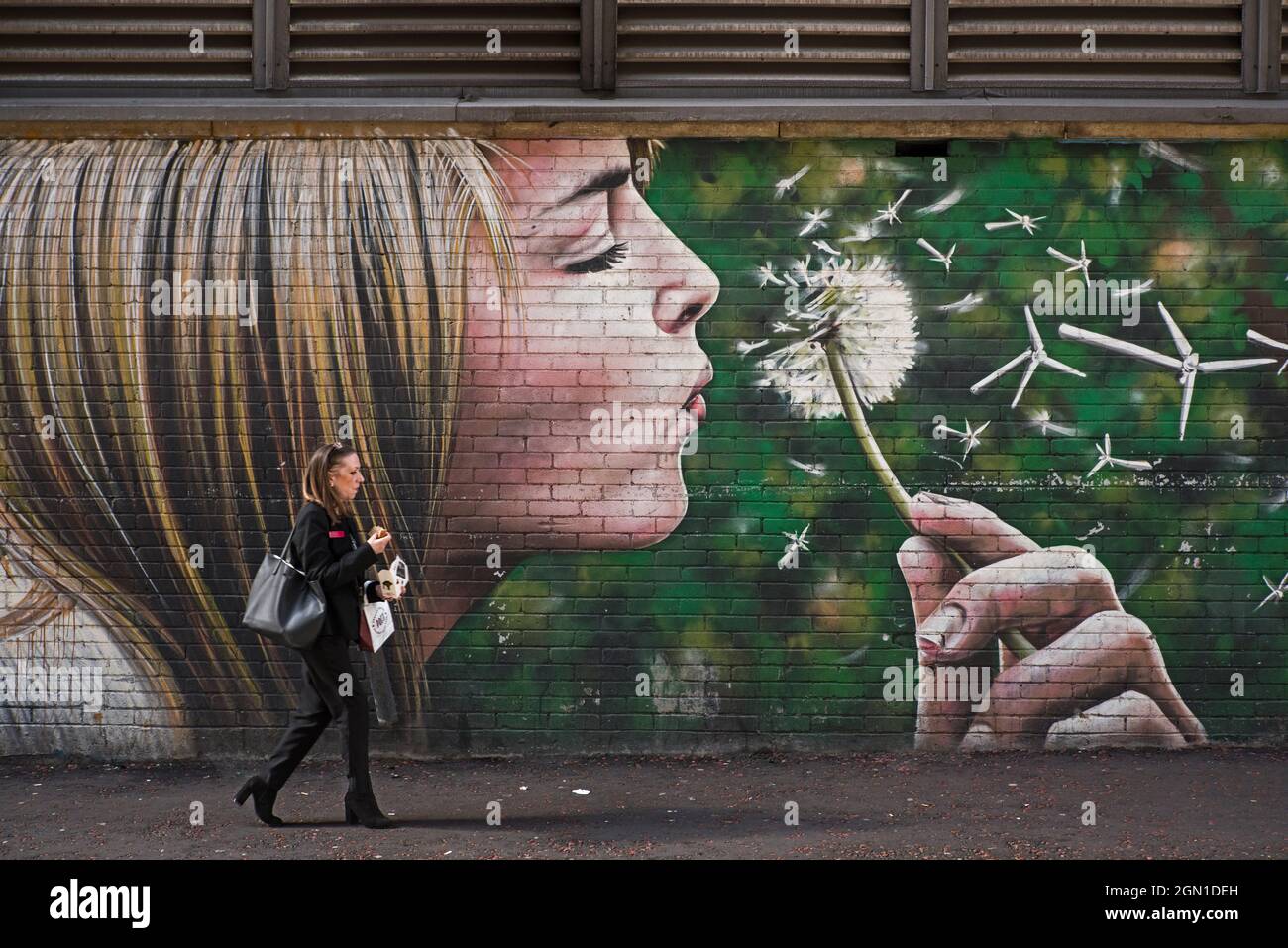 Femme marchant à côté de Wind Power, un morceau d'art de rue par Rogue-One et Art Pistol dans Mitchell Street, partie de la piste murale de Glasgow. Banque D'Images