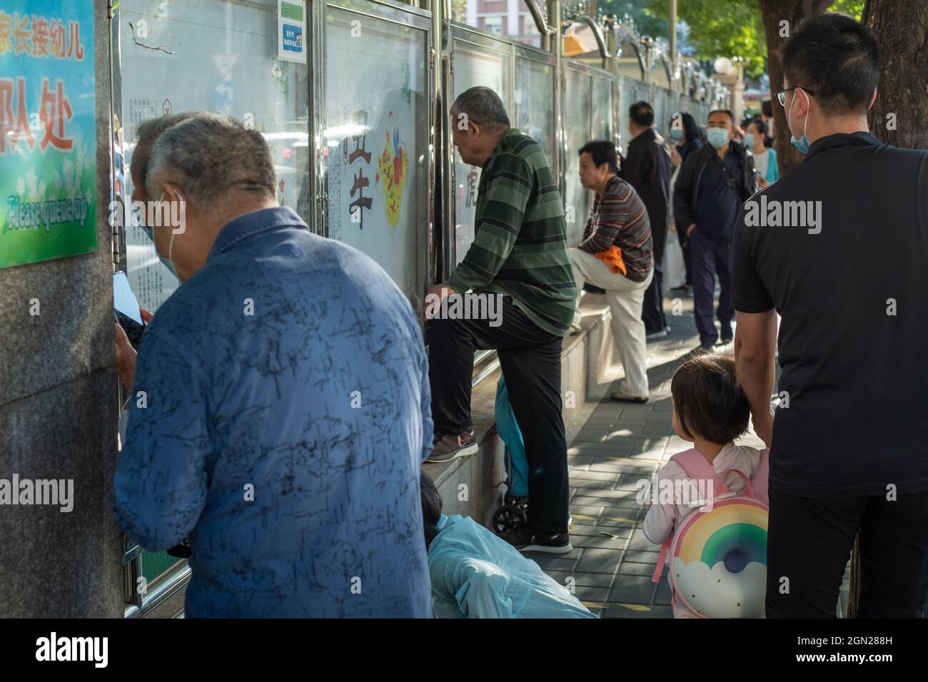 Les parents et les grands-parents qui prennent les enfants regardent leurs enfants dans la maternelle à travers les trous de clôture à Beijing, en Chine. 22 septembre 2021 Banque D'Images