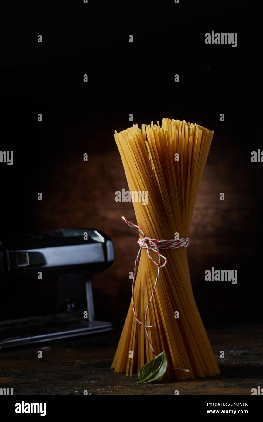 Bouquet de pâtes sèches placées avec une feuille de basilic sur une table en bois sur fond sombre en studio Banque D'Images