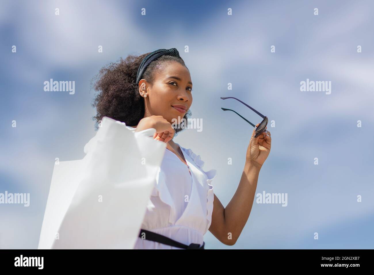 Jeune femme afro-américaine porte des lunettes de soleil et un sac blanc à l'extérieur. Banque D'Images