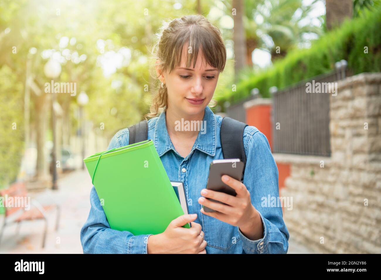 Jeune femme utilisant le mobile avec l'expression distraite tenant un dossier Banque D'Images
