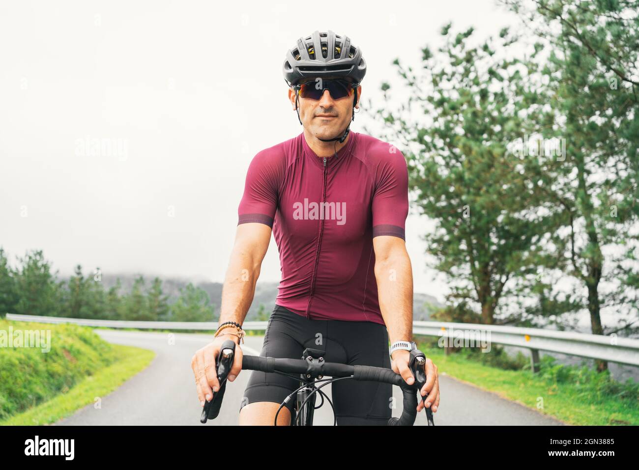 Sportif adulte en vélo lunettes de soleil et casque assis sur la route à vélo sur la route de campagne en plein jour Banque D'Images