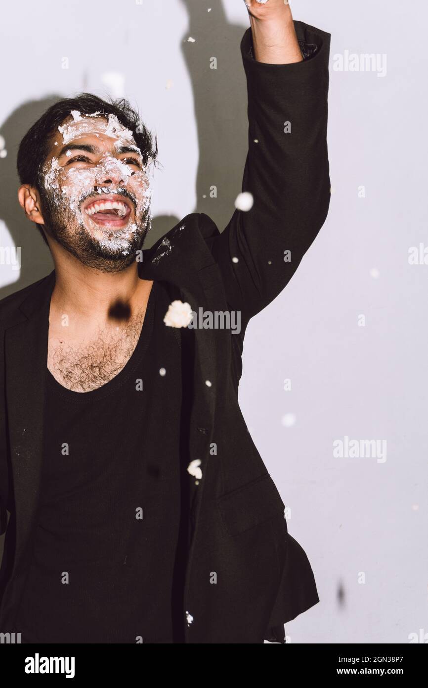 Un homme heureux avec un visage sale riant avec la bouche ouverte tout en jetant un gâteau d'anniversaire écrasé dans le studio Banque D'Images