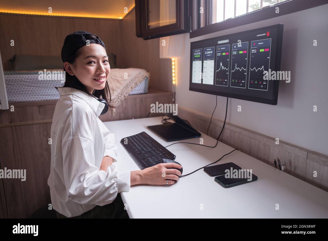 Vue latérale de la joyeuse femme asiatique travaillant sur ordinateur avec des graphiques montrant la dynamique des changements de valeur de la crypto-monnaie sur un lieu de travail pratique Banque D'Images