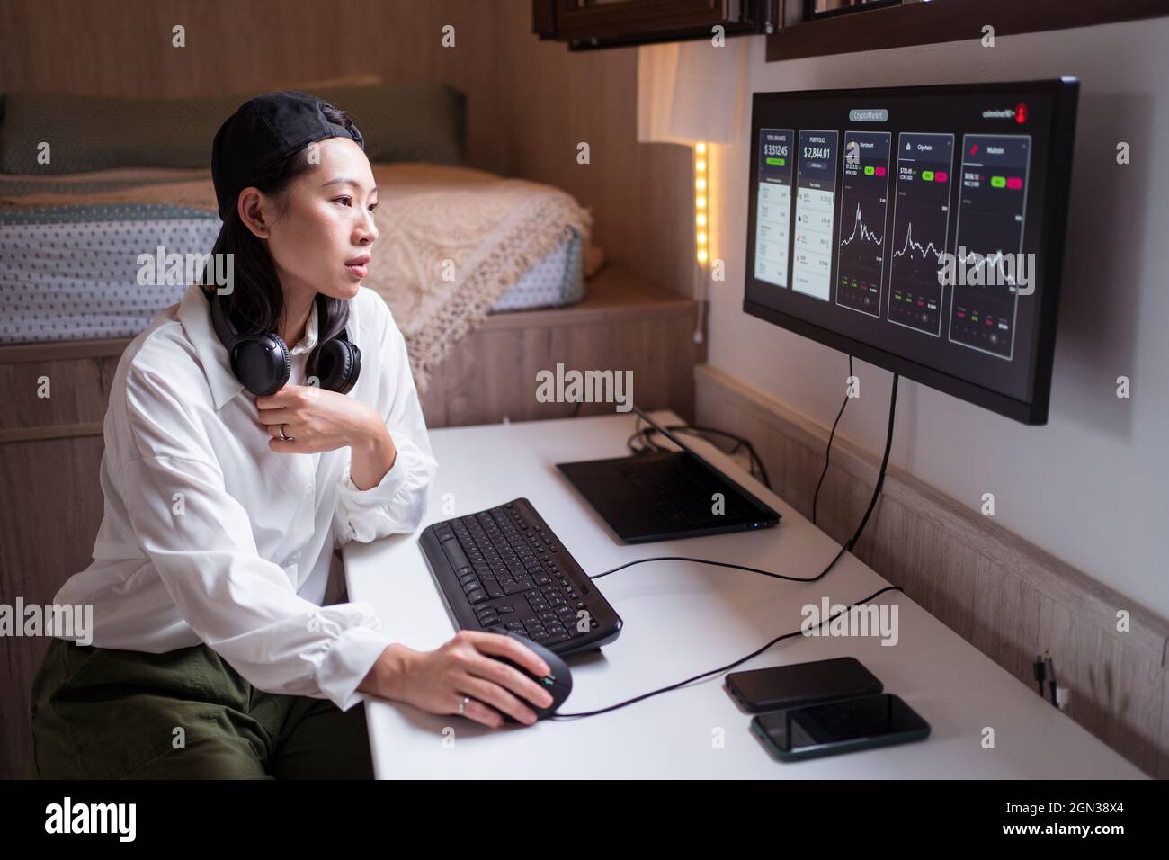 Vue latérale de la femme asiatique concentrée travaillant sur ordinateur avec des graphiques montrant la dynamique des changements de la valeur de la crypto-monnaie sur un lieu de travail pratique Banque D'Images
