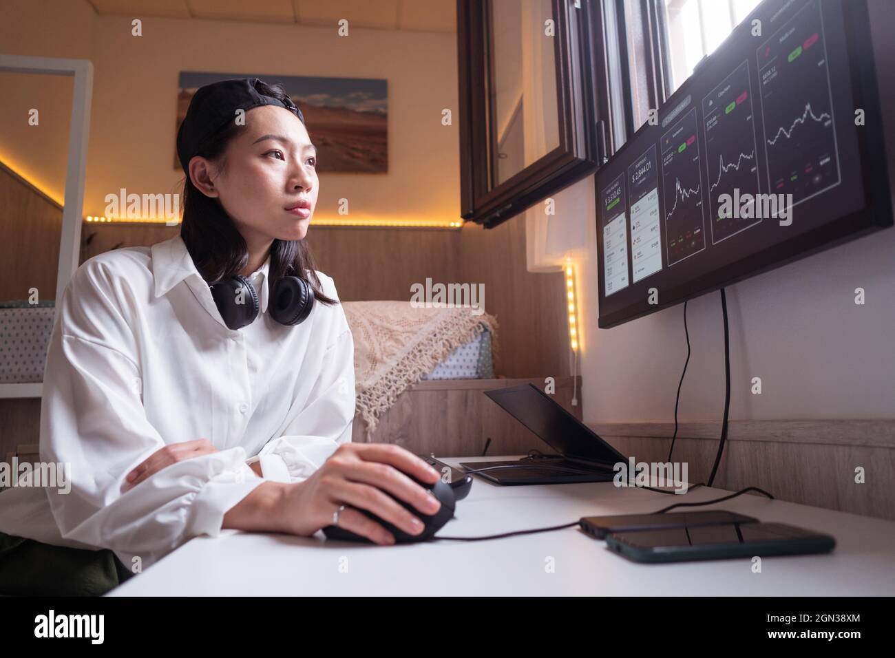 Vue latérale de la femme asiatique concentrée travaillant sur ordinateur avec des graphiques montrant la dynamique des changements de la valeur de la crypto-monnaie sur un lieu de travail pratique Banque D'Images