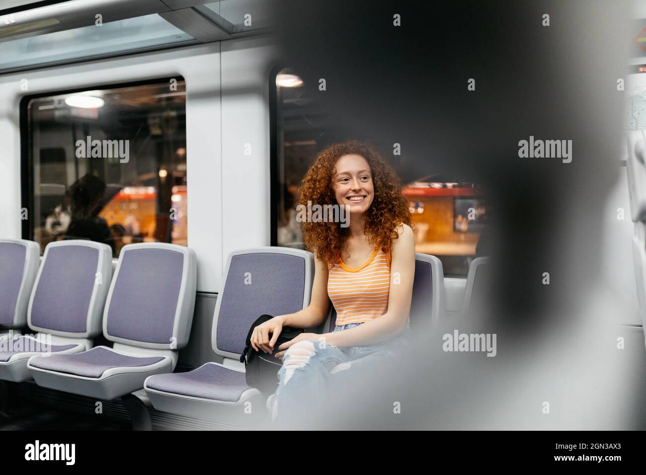 Contenu jeune femme en jeans déchirés avec cheveux rouge bouclés voyageant en train Banque D'Images