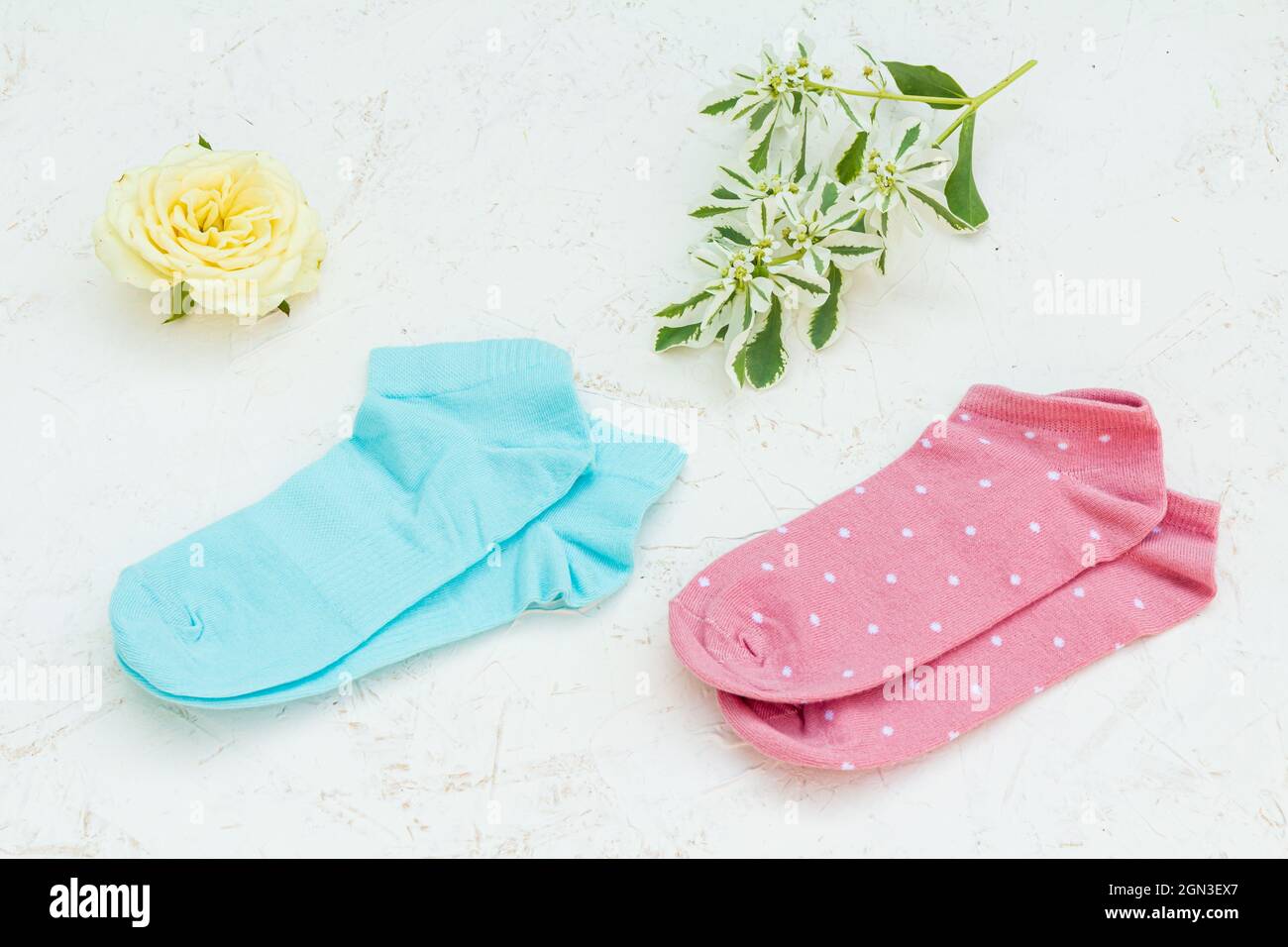Deux paires de chaussettes pour femmes et un bouton de rose sur le fond blanc structuré, vue du dessus. Banque D'Images