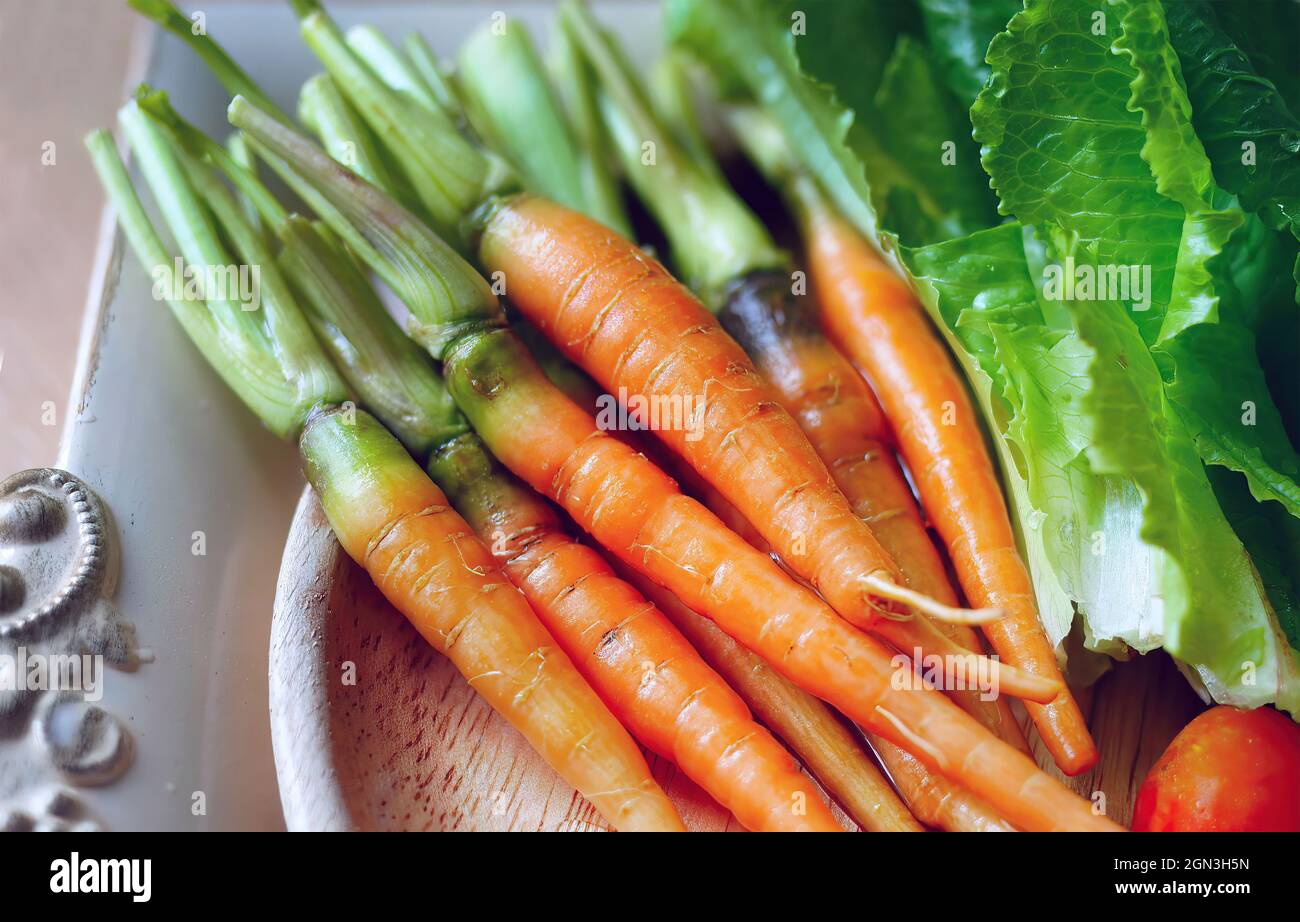 jeunes carottes fraîches de couleur orange sur le plateau en bois avec des légumes Banque D'Images