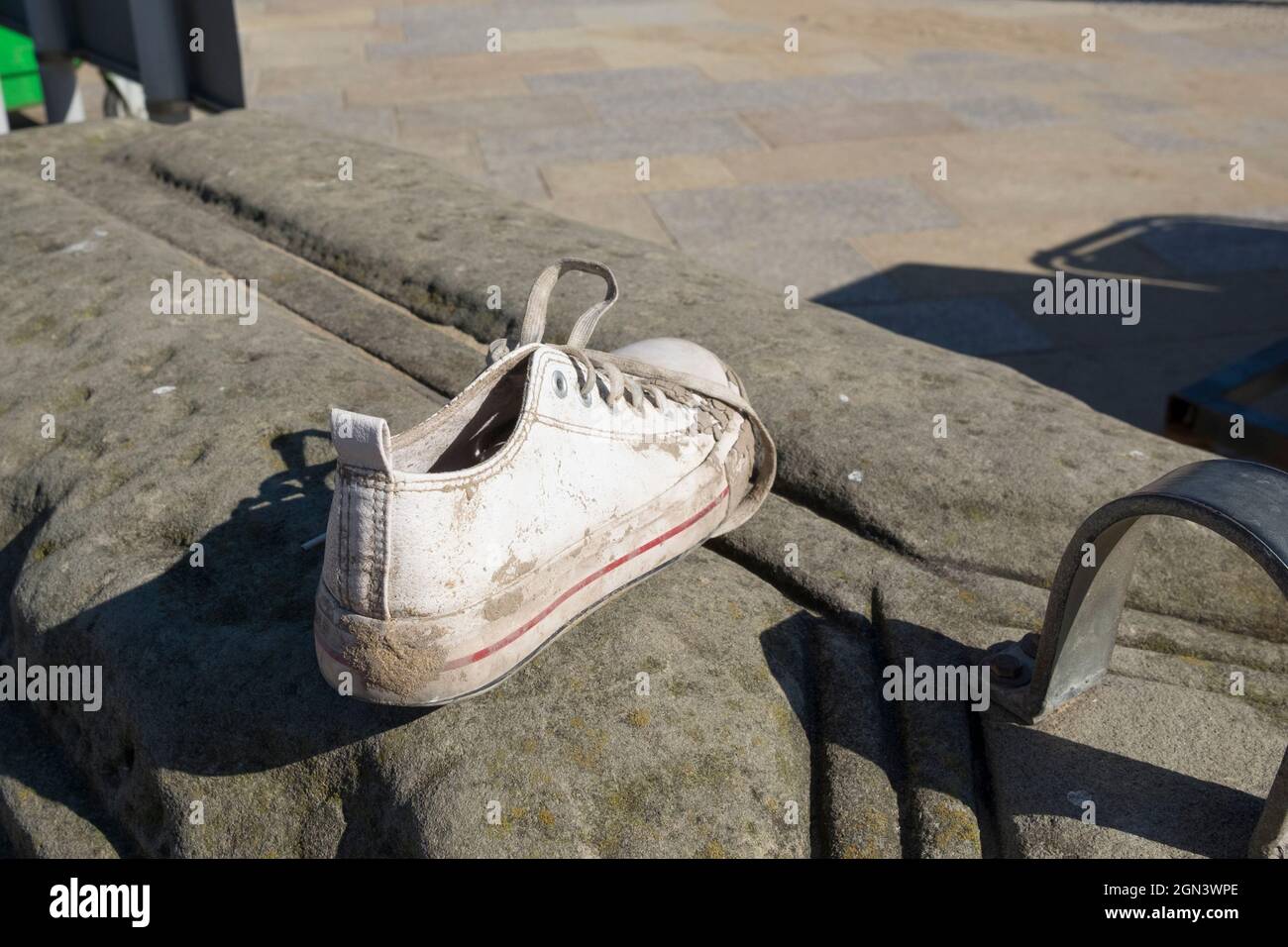 Un entraîneur, une chaussure de sport ou une sneaker, sur un mur de mer recouvert de sable sec, abondé ou perdu. Banque D'Images