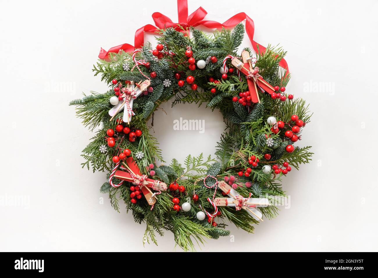 Couronne décorative de Noël de branche naturelle à feuilles persistantes avec baies de houx et ski sur fond blanc. Nouvelle année. Vue de dessus. Décoration traditionnelle Banque D'Images