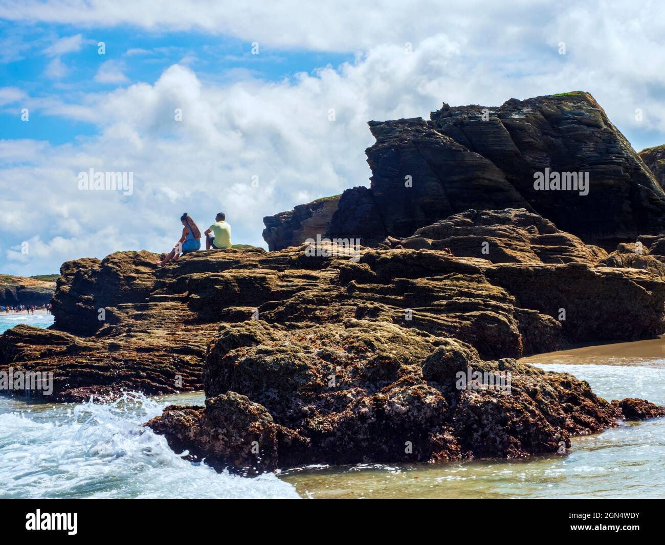 Ribadeo, Galice, Espagne. 07/26/2021 couple assis sur les rochers des falaises de la plage de Las Catedrales lors d'une journée d'été avec ciel bleu et nuages. Banque D'Images