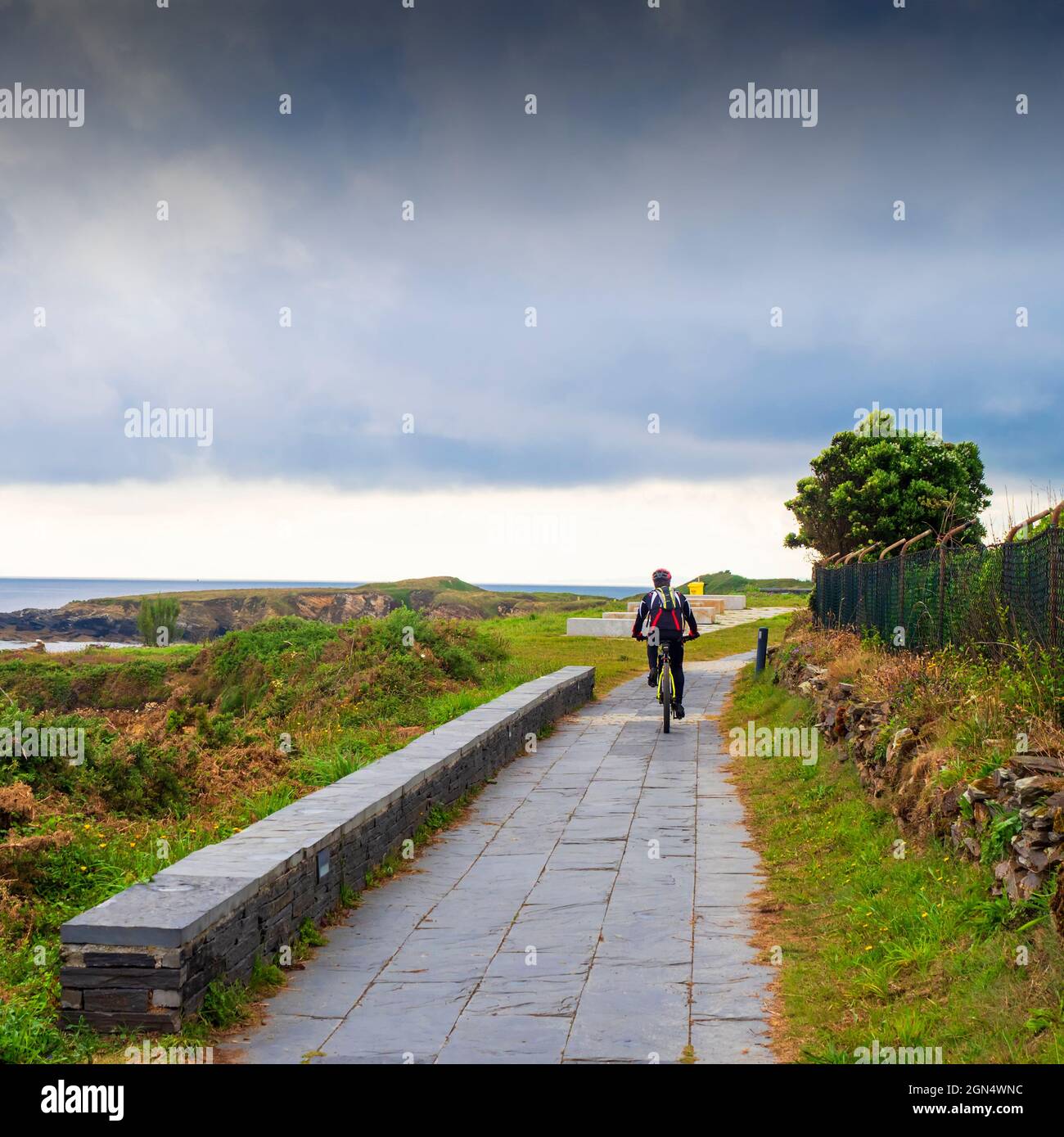 Un cycliste longeant une route au large de la côte de Playa de Las Catedrales à Lugo, Galice, lors d'une journée d'été nuageuse. Banque D'Images