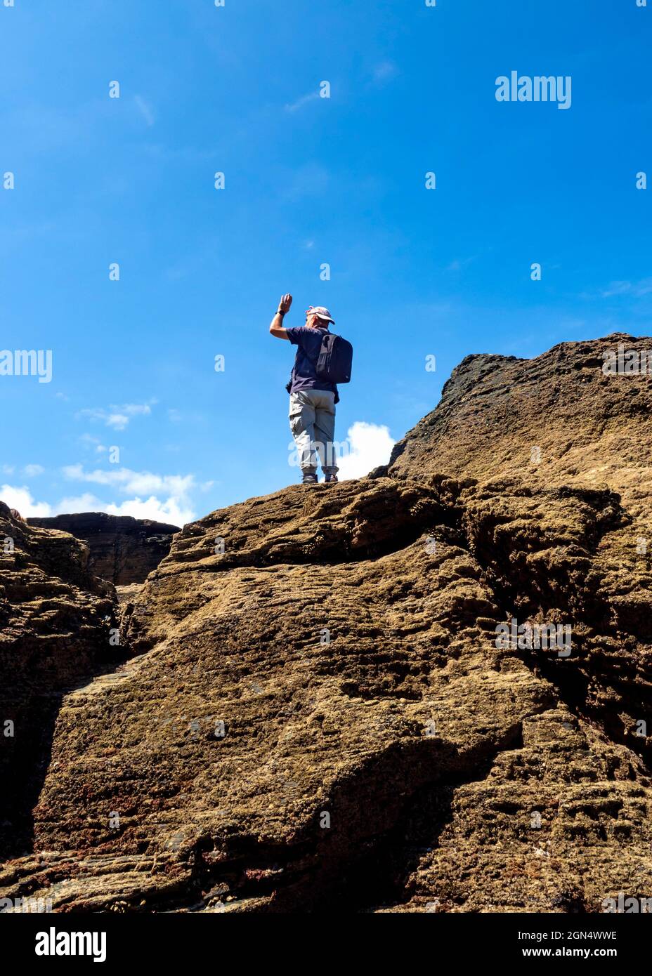 Un homme avec un sac à dos au sommet d'un pic sur les falaises de la plage de Las Catedrales à Ribadeo, un jour d'été avec un ciel bleu. Banque D'Images
