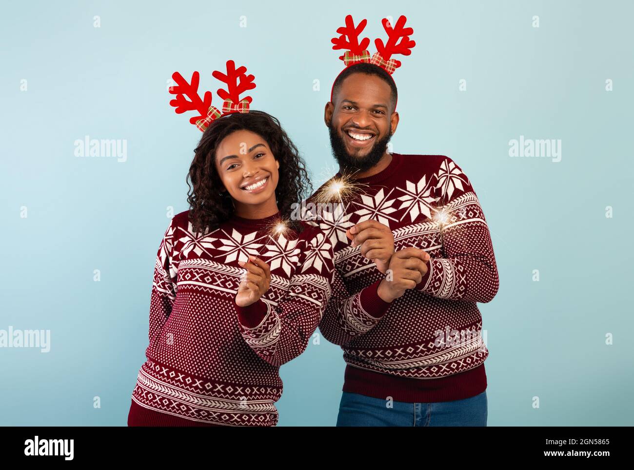 Célébration. Joyeux couple noir dans des cornes de cerfs et des chandails célébrant Noël ou le nouvel an avec des spamerons Banque D'Images