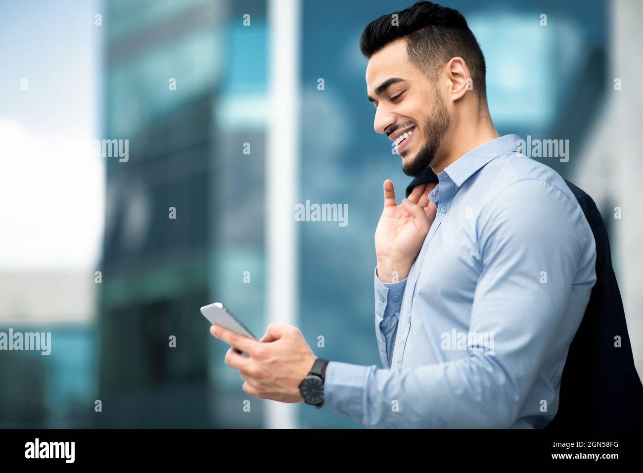 Vue latérale d'un jeune entrepreneur du Moyen-Orient qui vérifie ses e-mails sur son téléphone portable Banque D'Images