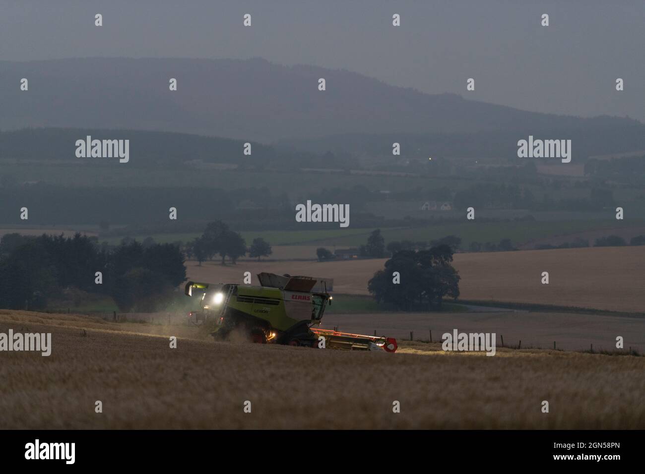 Vue sur la campagne de l'Aberdeenshire avec une moissonneuse-batteuse opérant dans un champ d'orge à Dusk Banque D'Images