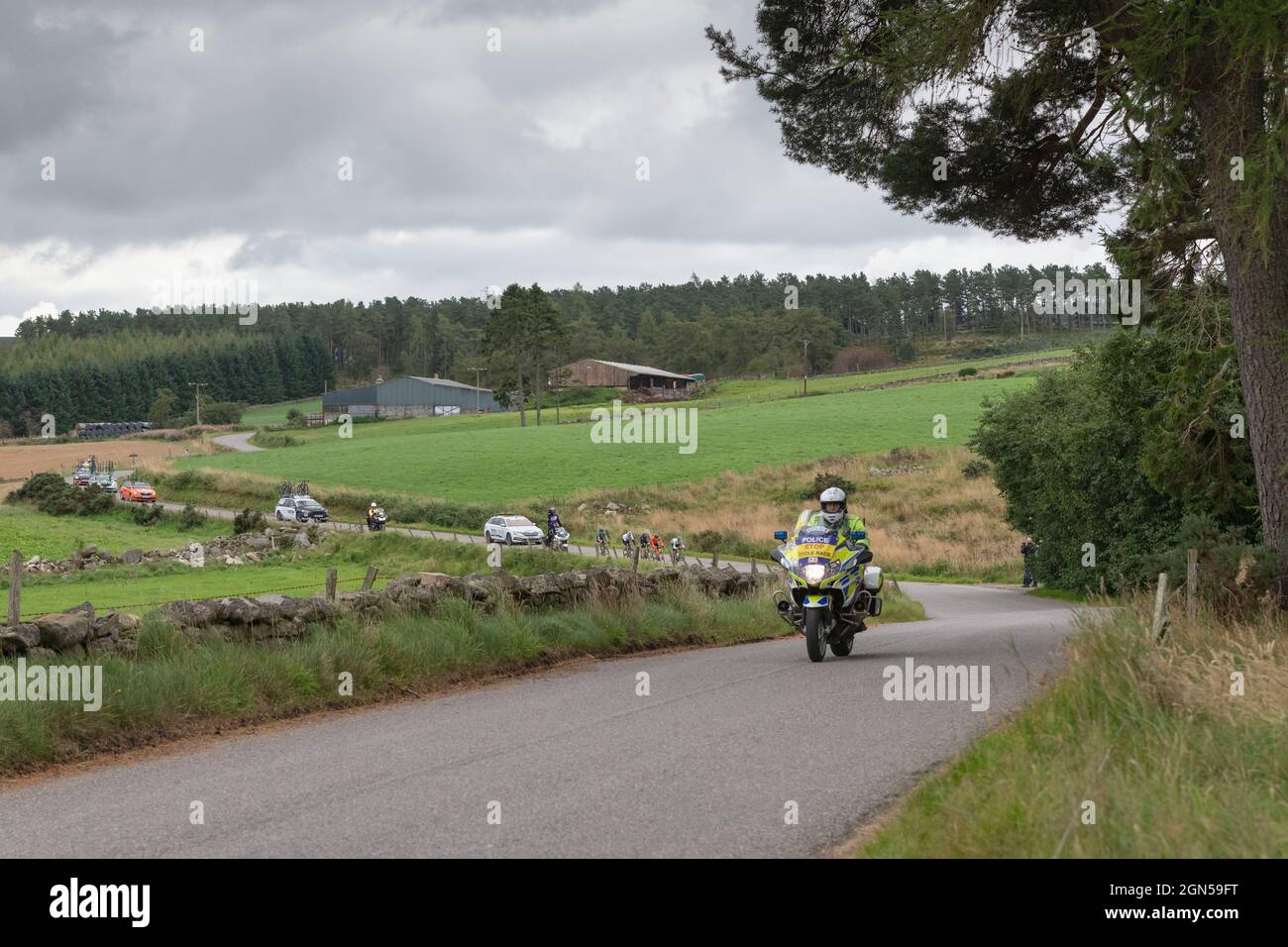 Une moto de police passe devant un petit break de cinq hommes dans le Tour de Grande-Bretagne de 2021 tandis qu'elle se déine dans la campagne de l'Aberdeenshire Banque D'Images