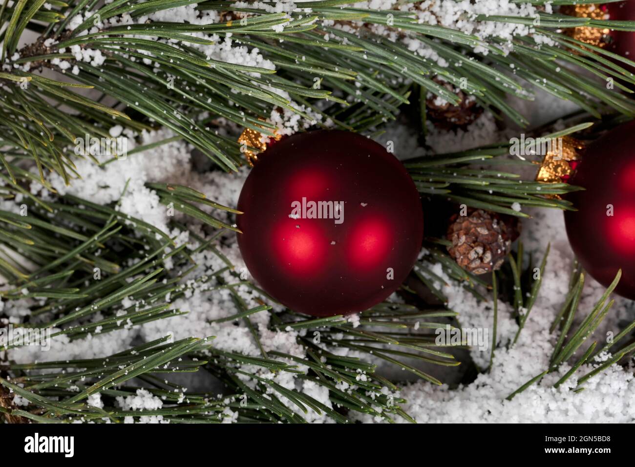 Vue rapprochée d'un ornement de boule rouge avec branches de sapin enneigées en arrière-plan pour un joyeux Noël ou de joyeuses fêtes du nouvel an Banque D'Images