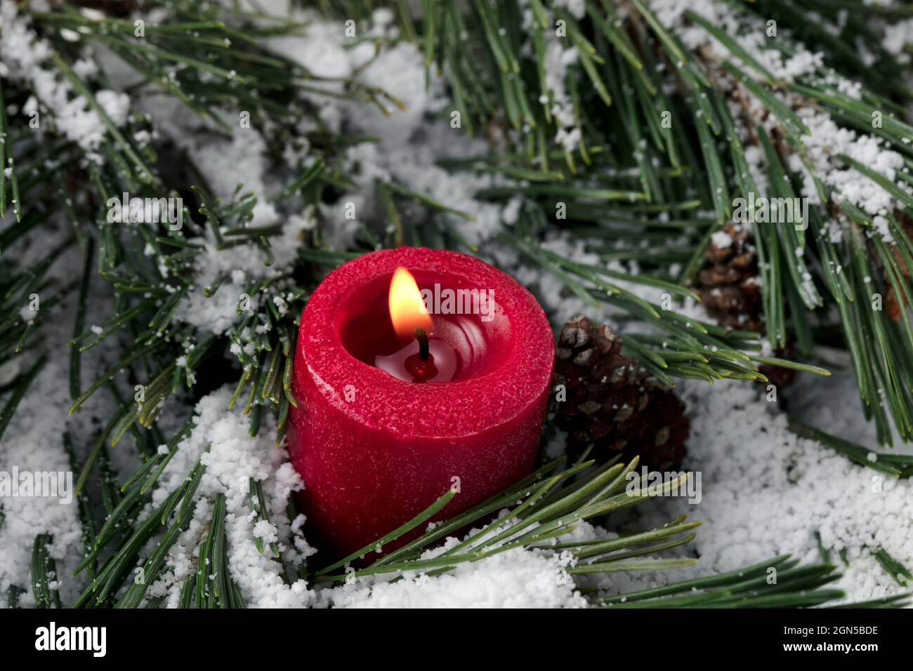 Vue rapprochée d'une bougie rouge brûlante avec branches de sapin enneigées en arrière-plan pour un joyeux Noël ou un joyeux Noël du nouvel an Banque D'Images