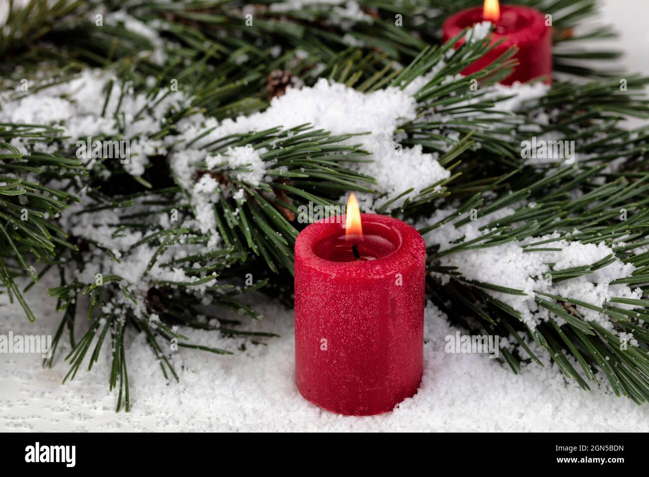 Vue rapprochée d'une bougie rouge lumineuse avec branches de sapin enneigées en arrière-plan pour un joyeux Noël ou une bonne fête du nouvel an Banque D'Images