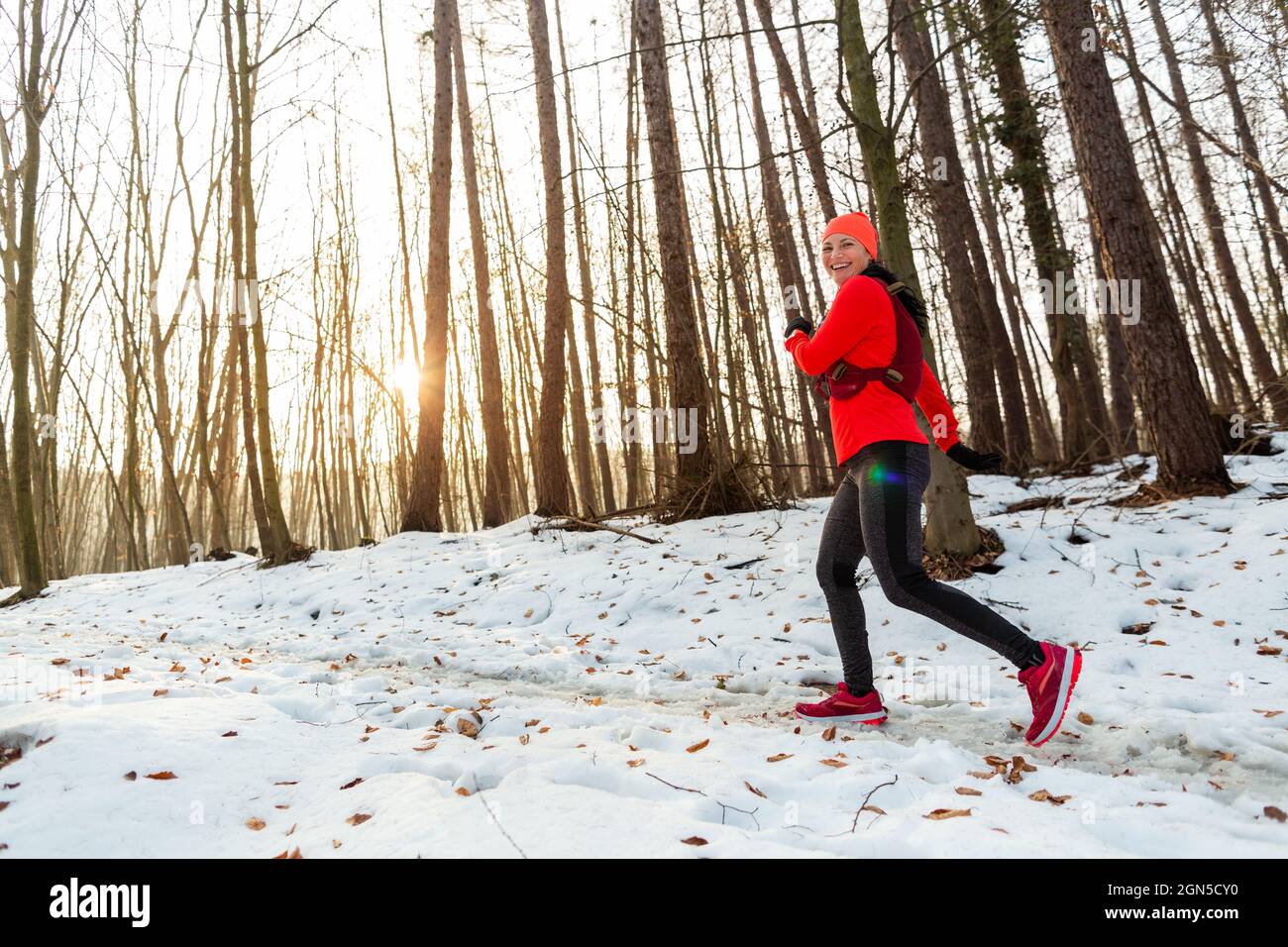 Femme en train de courir à travers les bois en hiver. Vue latérale du  coureur souriant portant un maillot de course à pied dans la forêt par  temps froid Photo Stock -