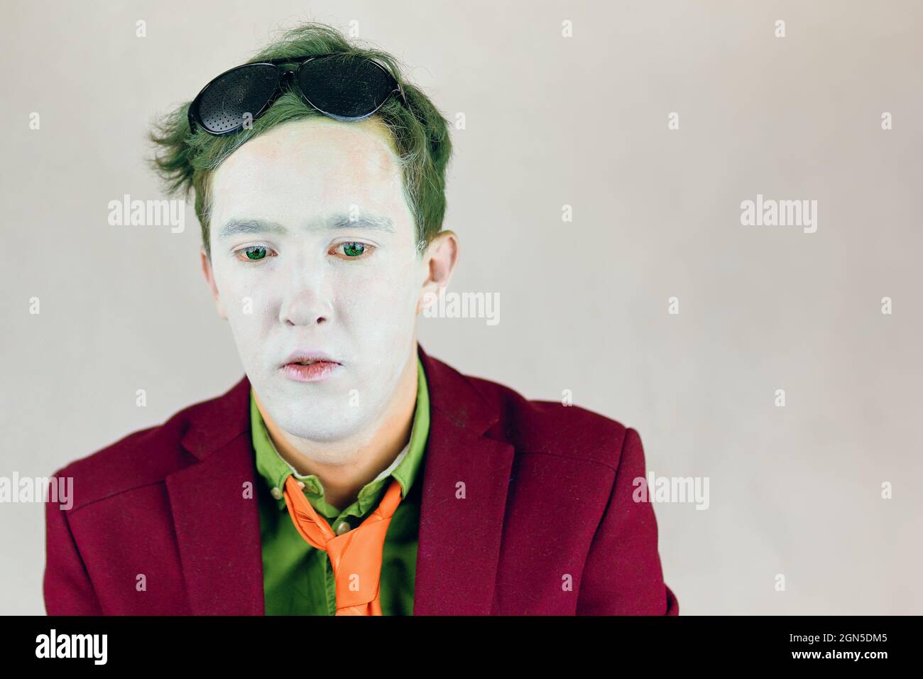 La personne en costume avec des rayures jaunes attache regarde vers le bas. Acteur avec maquillage blanc sur le visage et les yeux verts et les cheveux. Peinture de clown ou de mime. Concept de théâtre. Lunettes noires sur la tête. Banque D'Images