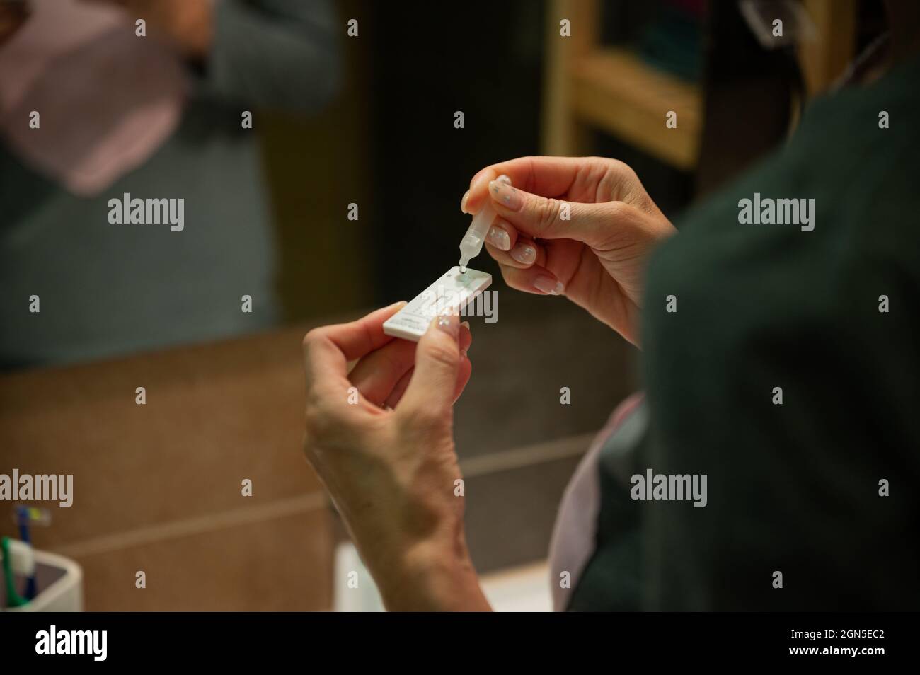 Vue sur l'épaule d'une femme faisant l'auto-test pour Covid 19, en laissant tomber la solution sur le bâton d'essai. Banque D'Images