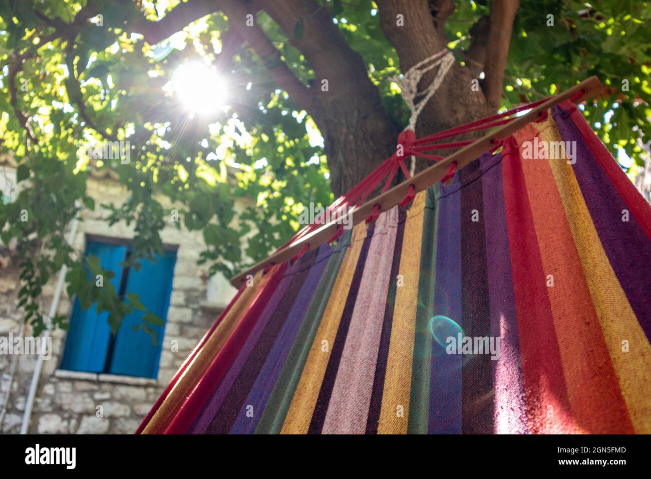 Balançant dans un hamac coloré avec le soleil brillant, branches d'arbre vertes, temps de détente d'été loisirs dans la cour traditionnelle grecque avec des murs de pierre Banque D'Images