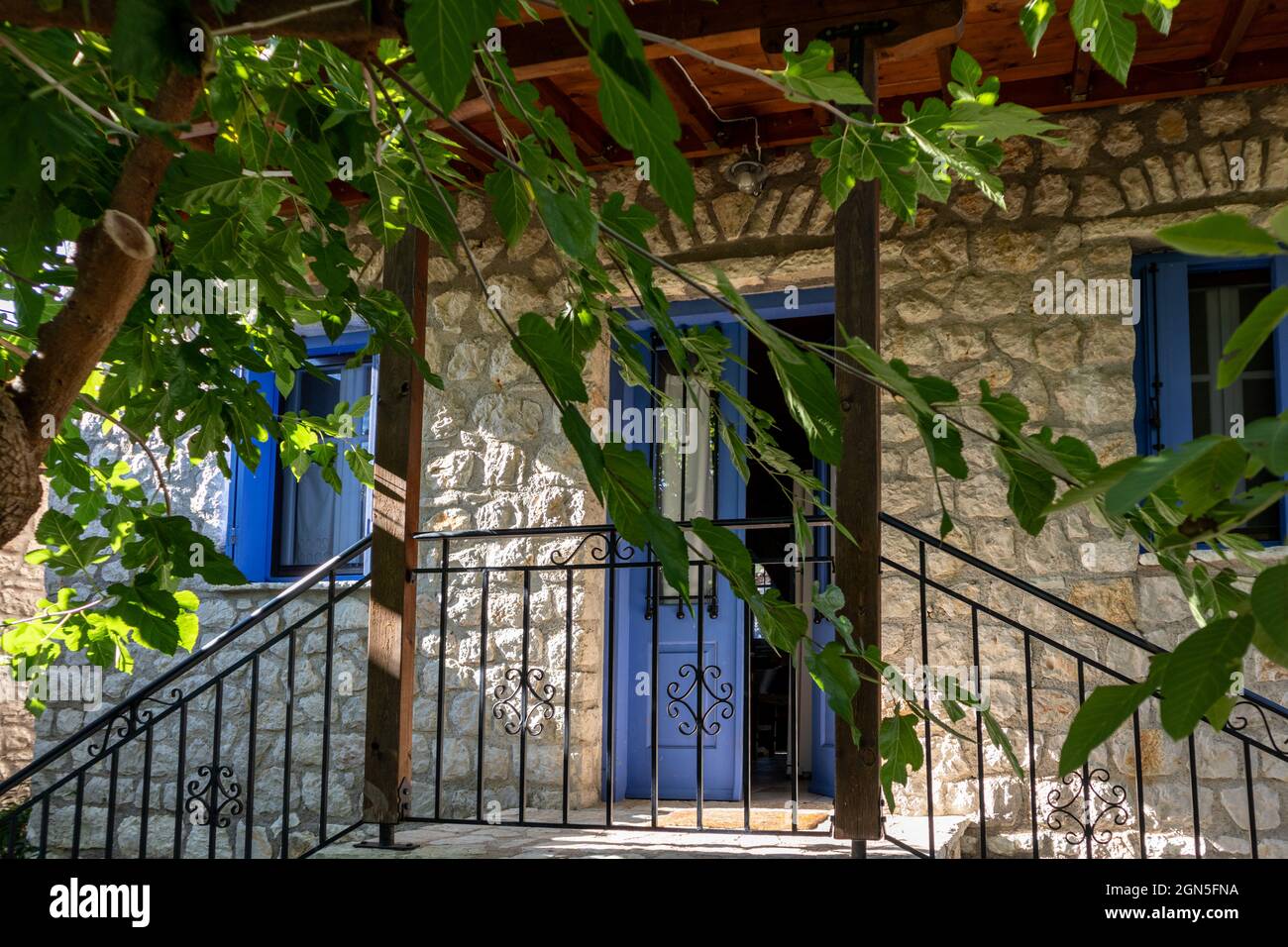 Soleil brillant à travers des branches d'arbres verts en été dans la cour traditionnelle grecque avec des murs en pierre, des portes bleues et des volets de fenêtres. Lieu de voyage d'été Banque D'Images