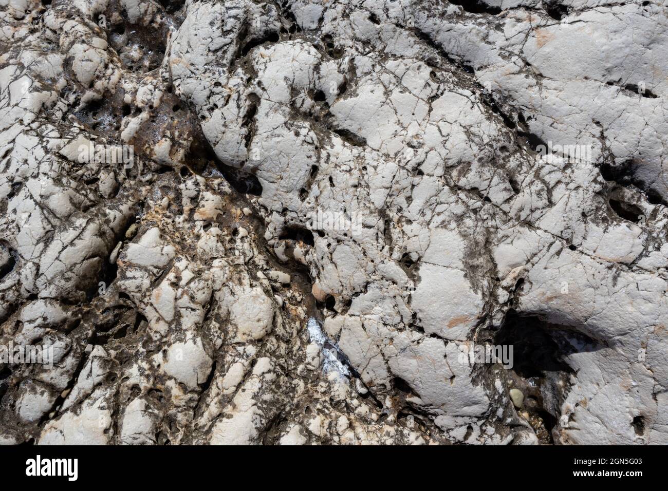 Roche en marbre naturel blanc et noir avec texture de gros plan craquelée. Détails de la surface en pierre claire dans la Grèce ensoleillée Banque D'Images