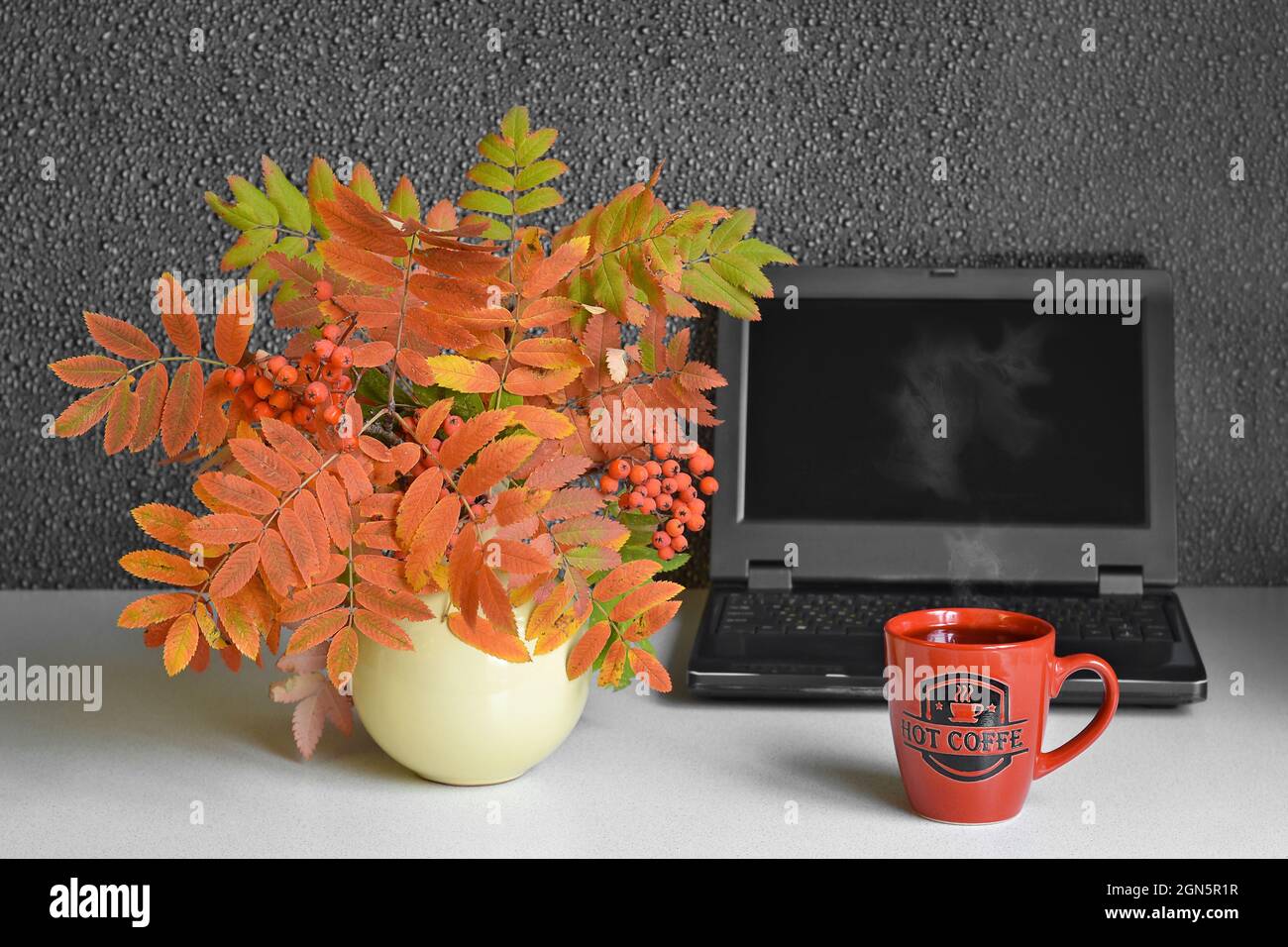 Une tasse de café chaud à la vapeur, sur le fond d'un ordinateur et d'un bouquet de feuilles d'automne Banque D'Images
