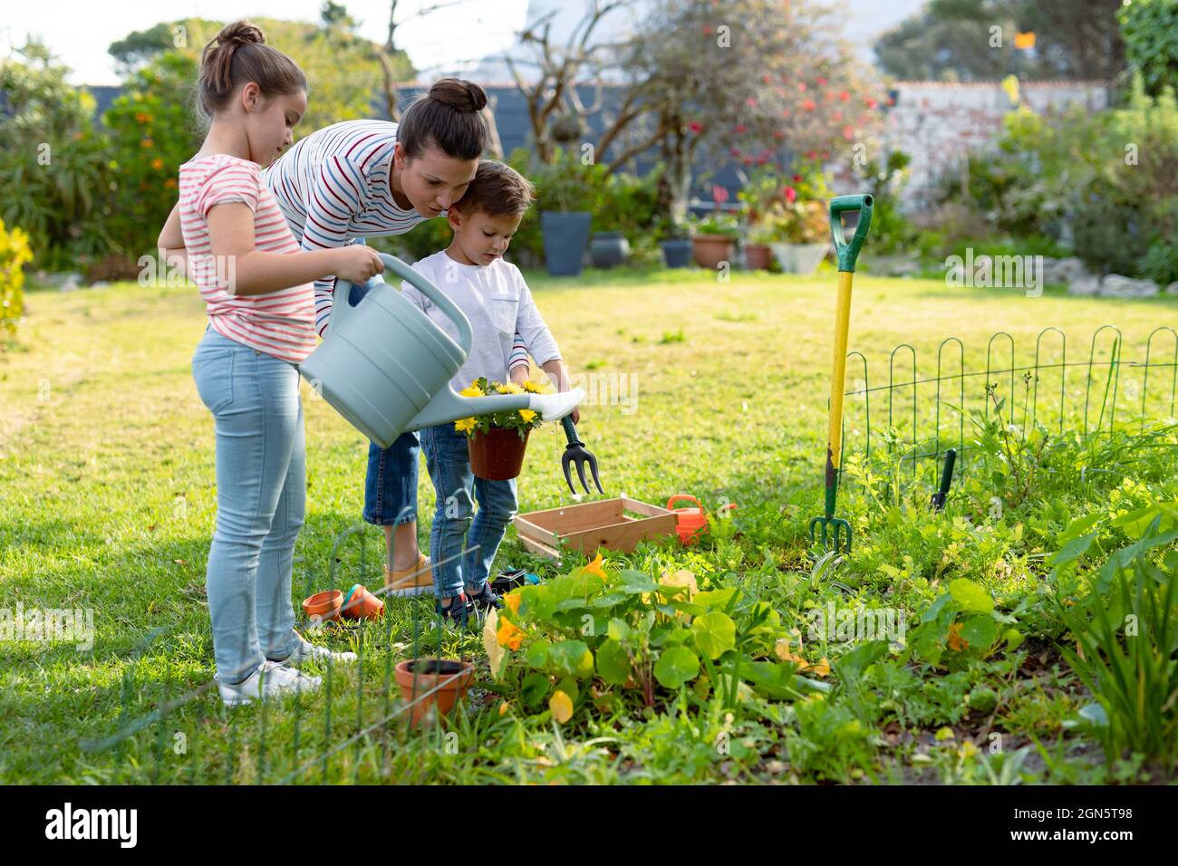 Bonne mère, fille et fils caucasiens arroser les plantes ensemble Banque D'Images