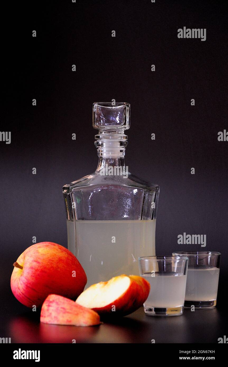 Calvados de pomme, un alcool fort dans une bouteille de verre et deux  verres avec des morceaux de fruits sur un fond noir. Gros plan Photo Stock  - Alamy