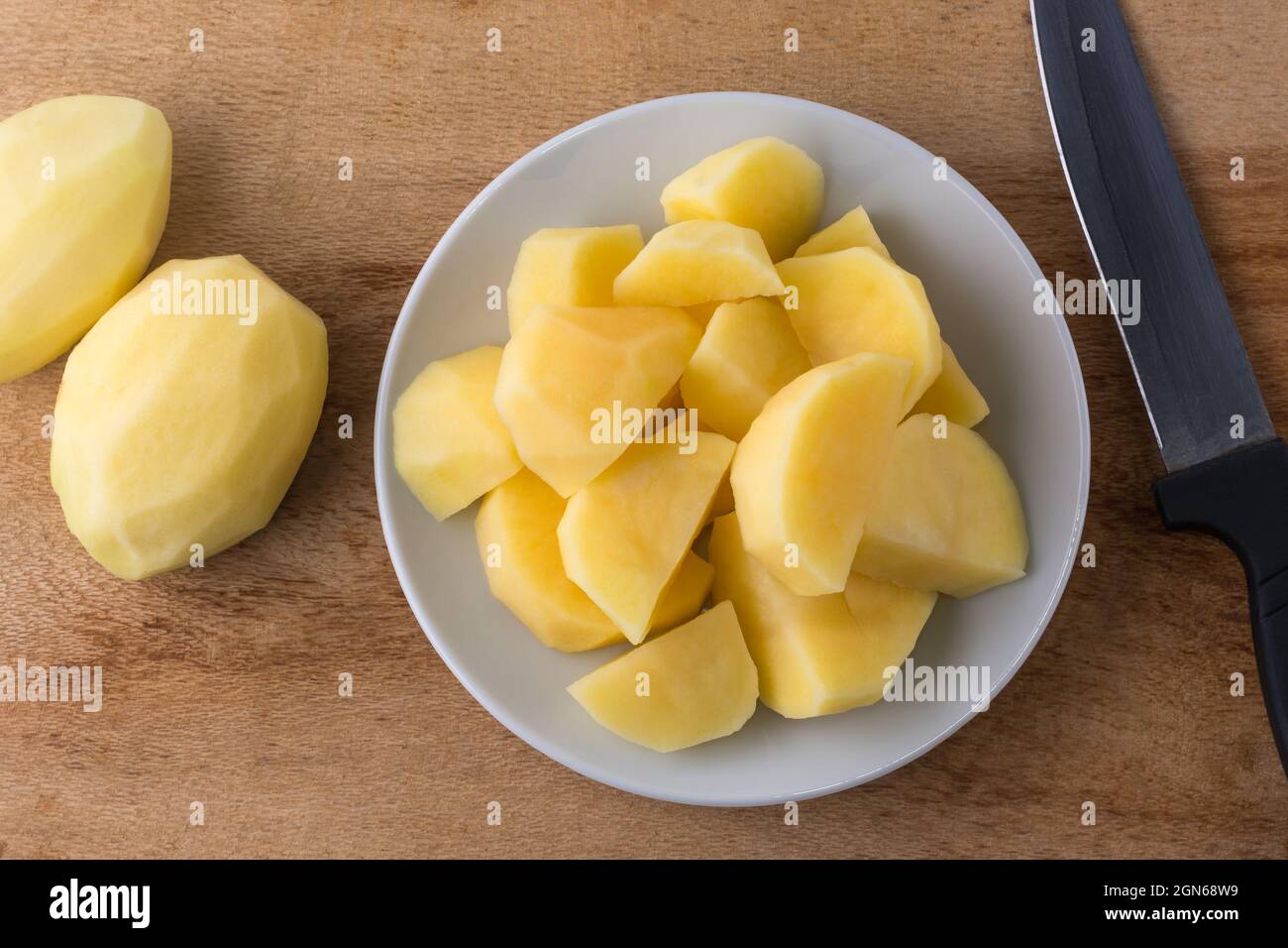 pommes de terre crues hachées sur une assiette blanche, avec un couteau et des pommes de terre entières pelées sur le fond, vue rapprochée prise de dessus Banque D'Images