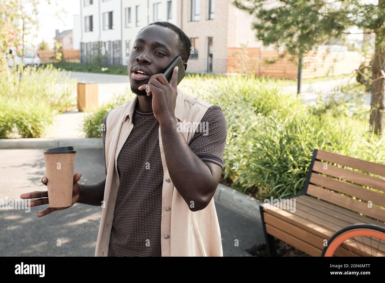 Portrait horizontal moyen de beau jeune Noir homme passant du temps à l'extérieur à marcher, boire du café et parler au téléphone avec quelqu'un Banque D'Images