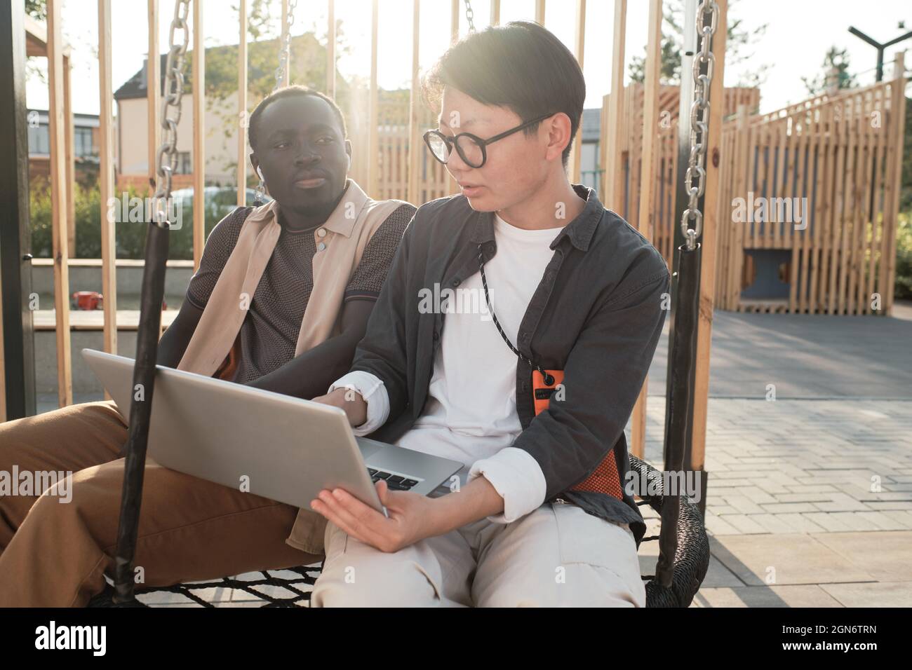 Portrait horizontal moyen d'un beau homme afro-américain et d'une élégante femme asiatique assis ensemble dans un parc urbain travaillant sur un projet important Banque D'Images