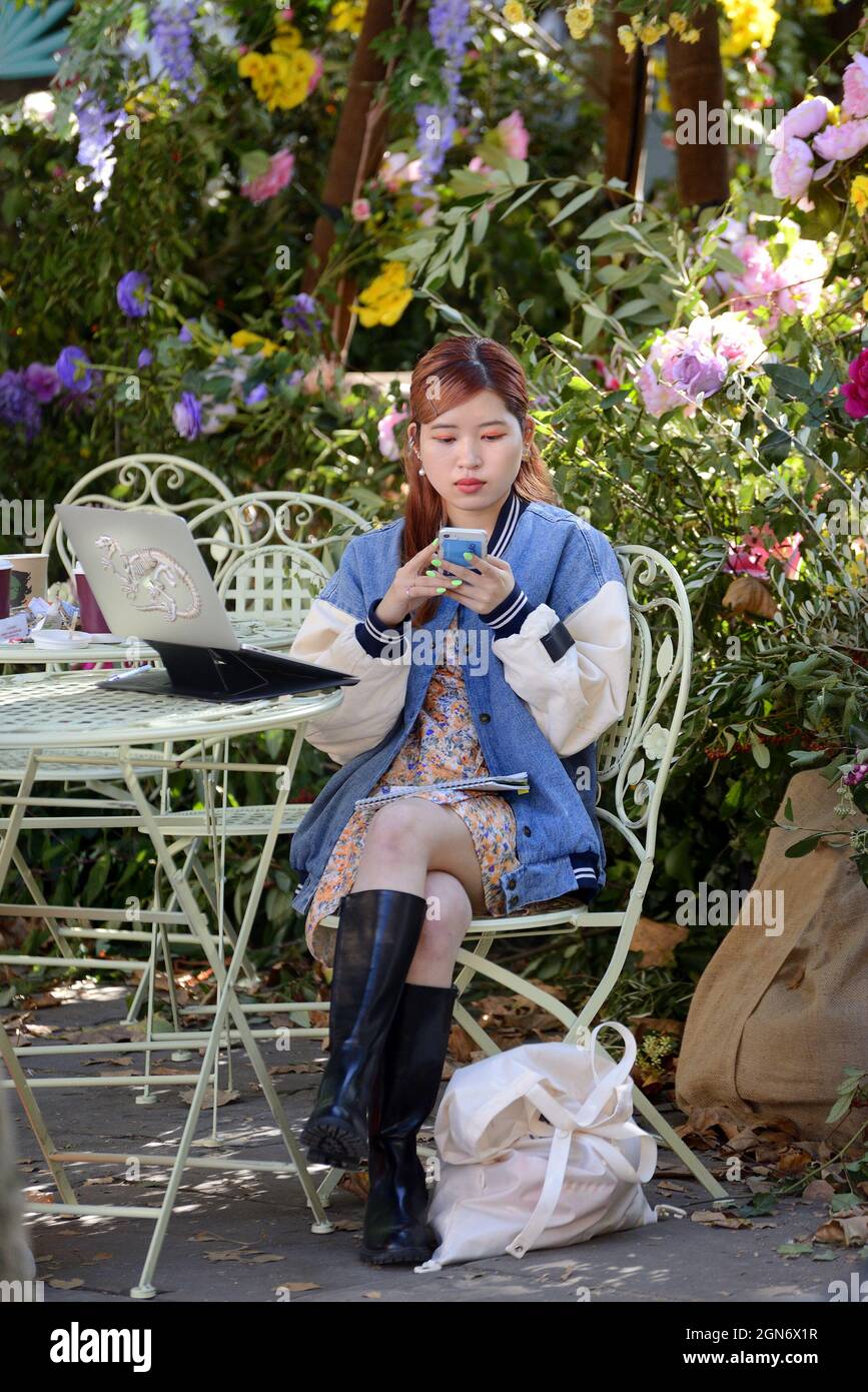 Londres, Angleterre, Royaume-Uni. Jeune femme asiatique sur son téléphone mobile, assise avec son ordinateur portable, à Sloane Square, pendant Chelsea dans Bloom 2021 Banque D'Images