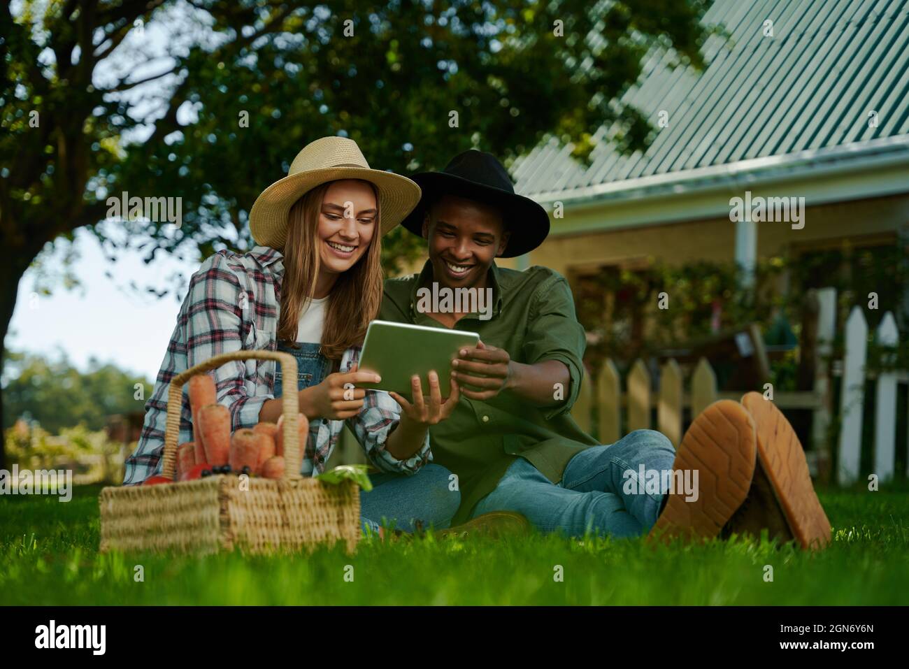 Fermiers mixtes de race masculine et féminine assis dans la lecture de l'herbe sur la tablette numérique Banque D'Images