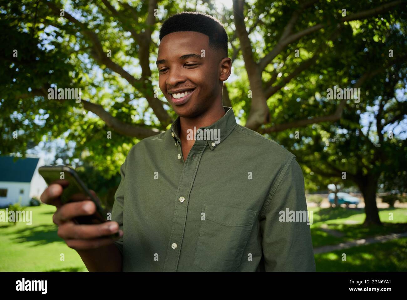 Fermier masculin de race mixte debout à l'extérieur souriant à l'appareil cellulaire Banque D'Images