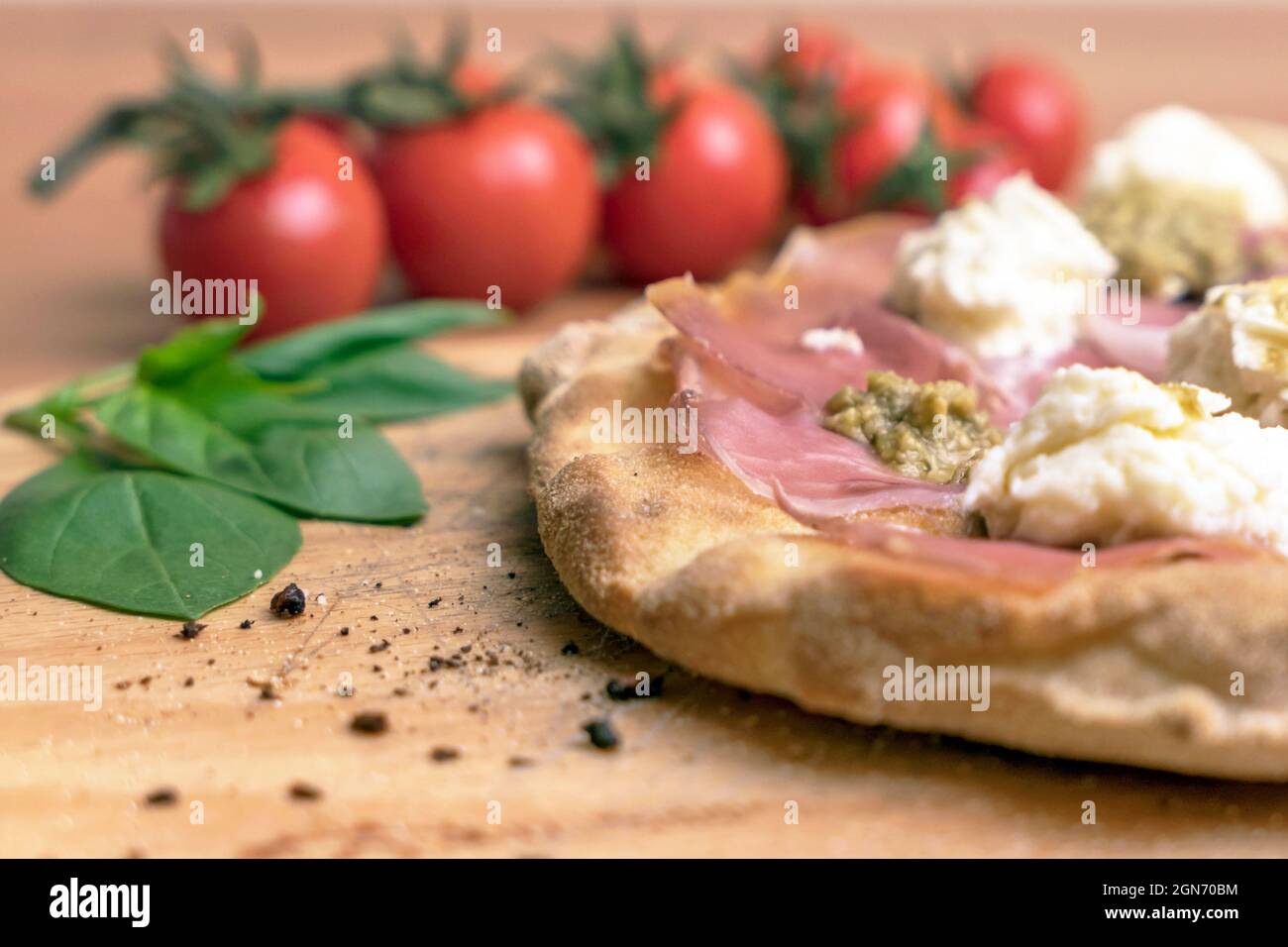 Gros plan de la pizza italienne sur une planche à découper en bois. Sur fond tomates et basilic défocused. Banque D'Images
