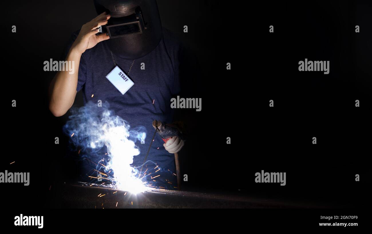 Travailleur de l'industrie des métaux avec une étiquette de cou de personnel, soudant la tôle dans une usine. Eclaircissement sur fond sombre, gros plan. Travail intensif en usine. Banque D'Images