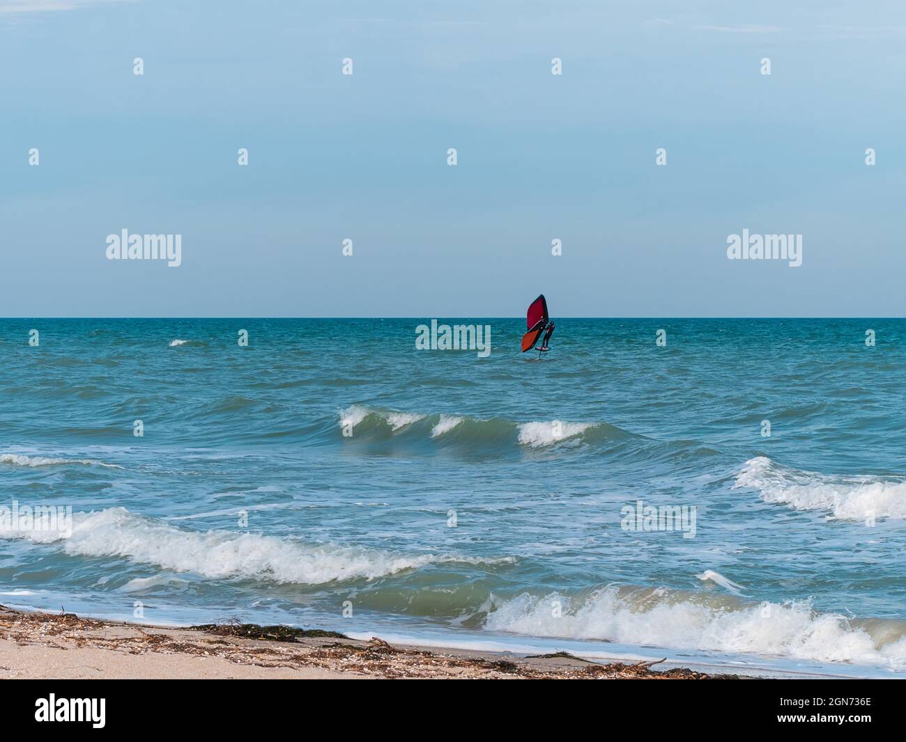 L'athlète est à cheval sur une planche de surf hydrofoil à l'aide d'une aile de papier d'aluminium à main sur les vagues de l'océan. Sports extrêmes d'automne. Vacances en mer d'automne. Temps venteux sur le Banque D'Images