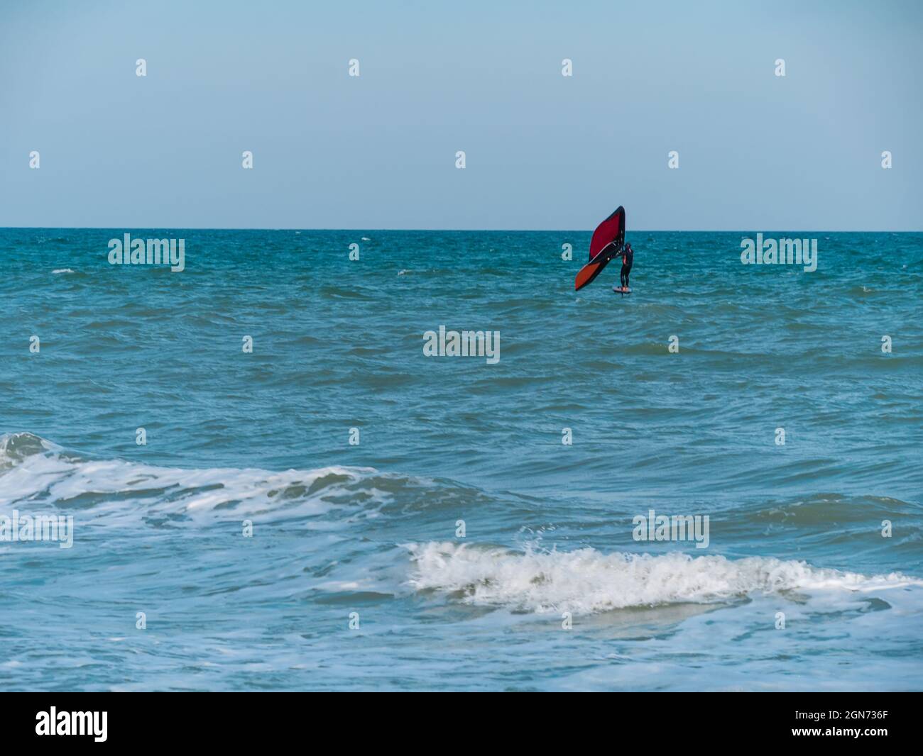 L'athlète est à cheval sur une planche de surf hydrofoil à l'aide d'une aile de papier d'aluminium à main sur les vagues de l'océan. Sports extrêmes d'automne. Vacances en mer d'automne. Temps venteux sur le Banque D'Images