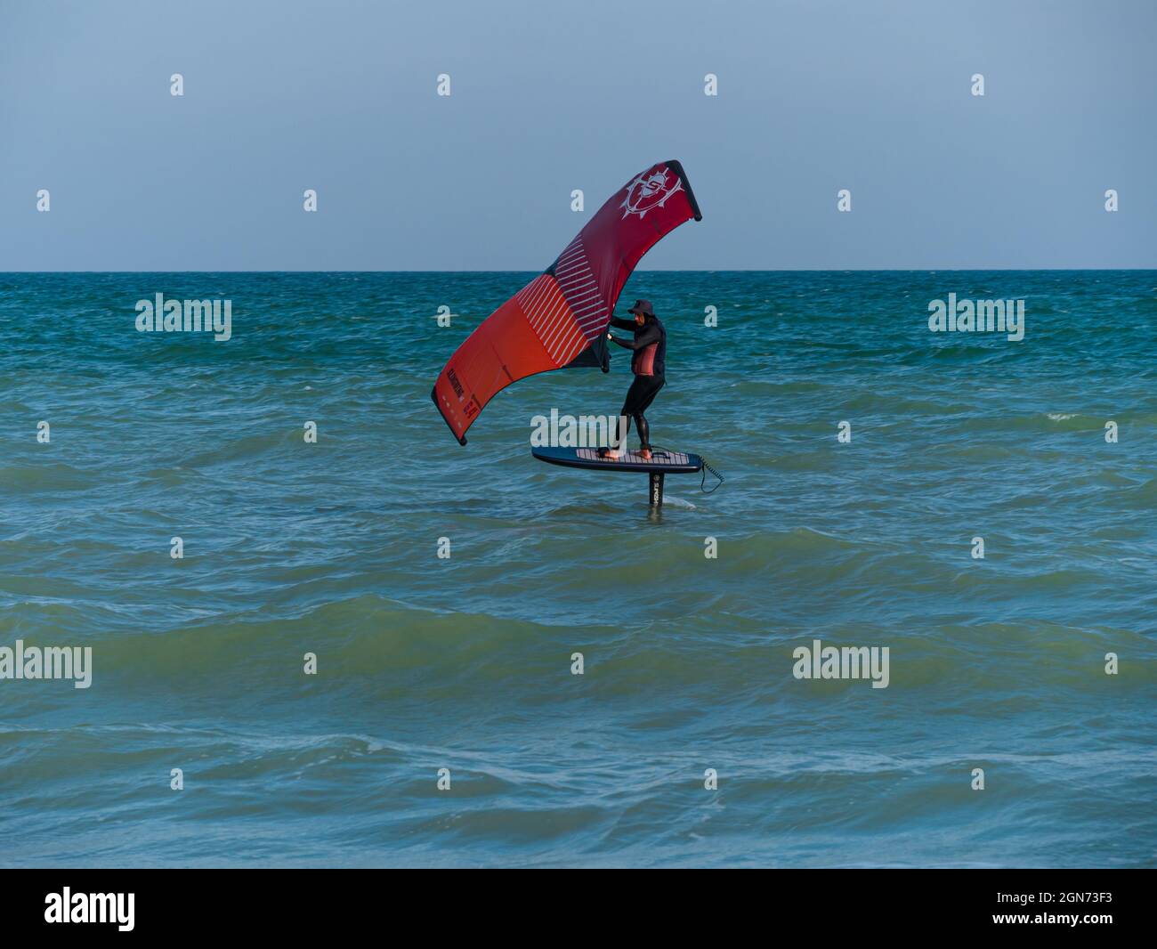 L'athlète est à cheval sur une planche de surf hydrofoil à l'aide d'une aile de papier d'aluminium à main sur les vagues de l'océan. Sports extrêmes d'automne. Vacances en mer d'automne. Temps venteux sur le Banque D'Images