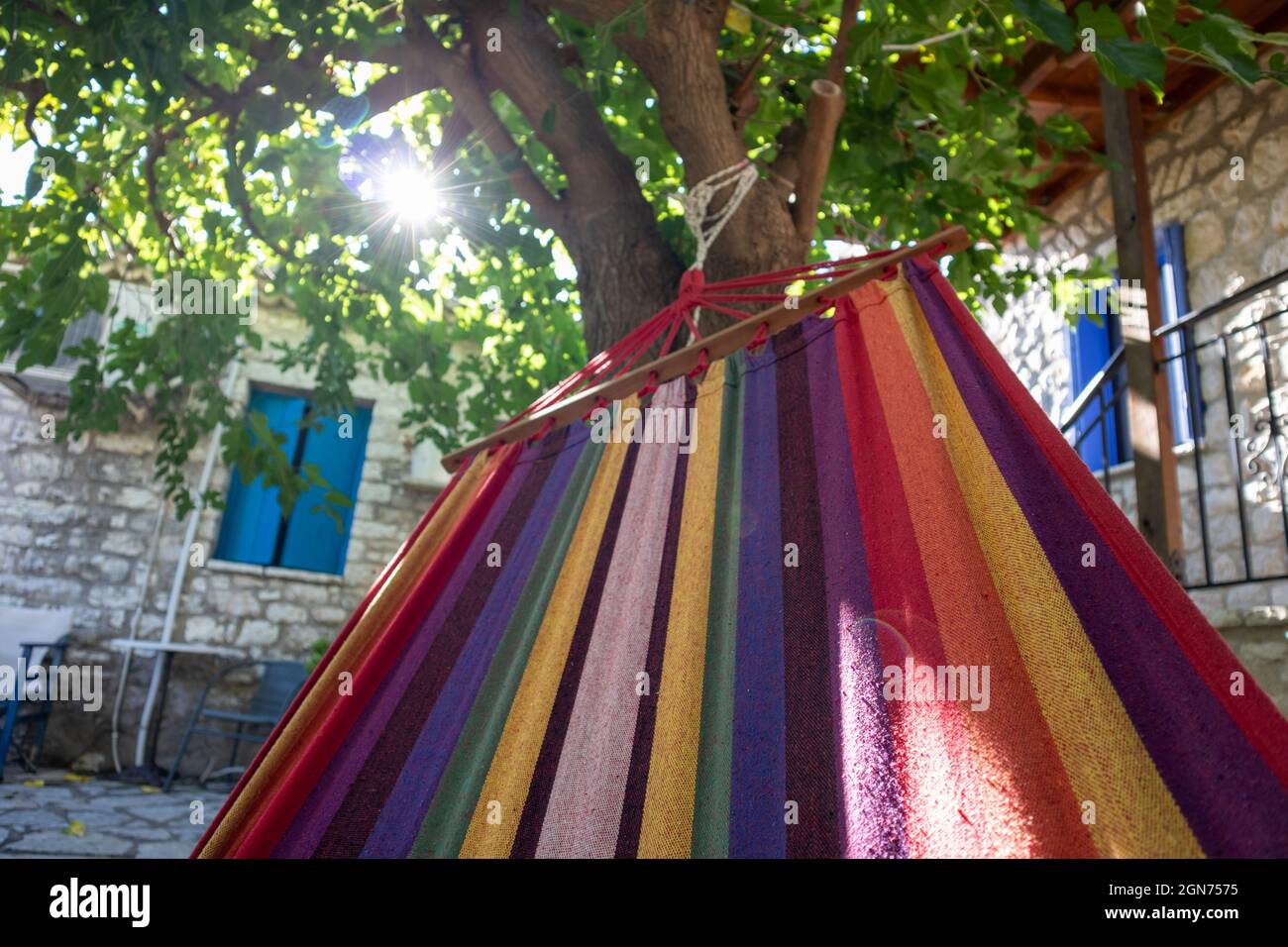 Balançant dans un hamac coloré avec le soleil briller à travers des branches d'arbre vertes, temps de loisirs d'été dans la cour traditionnelle grecque de maison avec des murs de pierre et Banque D'Images