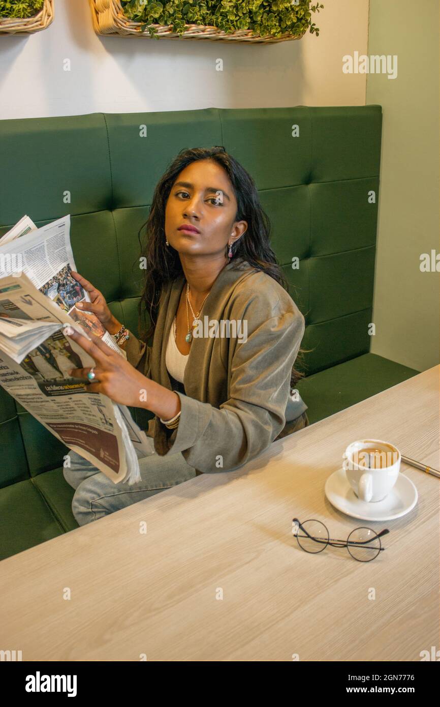 Femme noire tenant un journal tout en prenant le petit déjeuner dans une cafétéria avant de commencer à travailler. Concept de la vie étudiante 2021. Banque D'Images