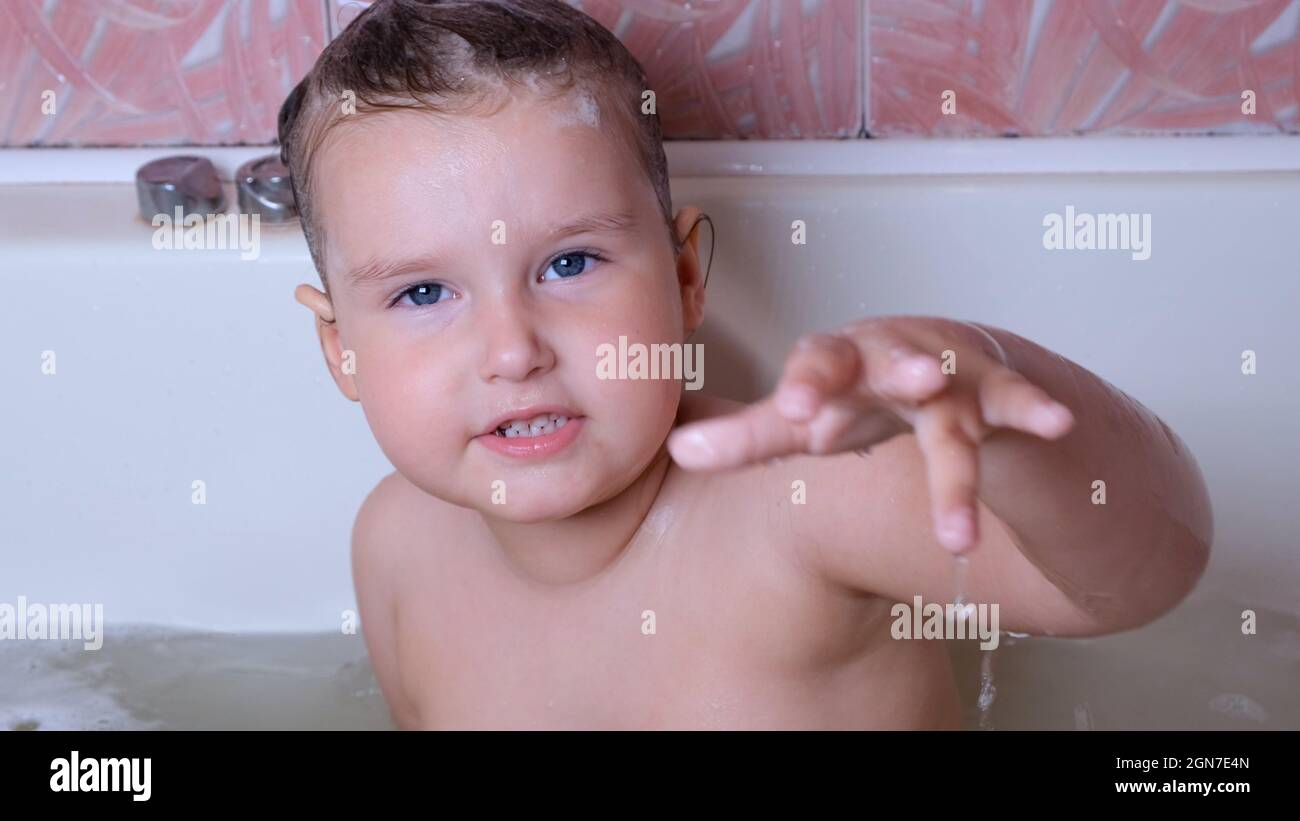 Petite fille de jeu 3 ans bain et lave avec de la mousse sur sa tête dans  l'eau dans la salle de bains à la maison. Concept de soins du corps de